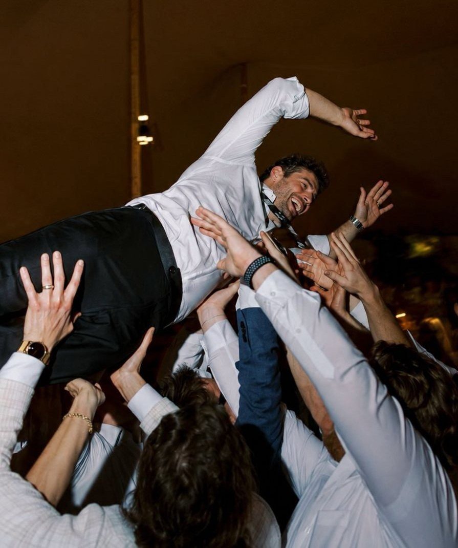 Wedding guests lifting a celebrating guest into the air, every hand free